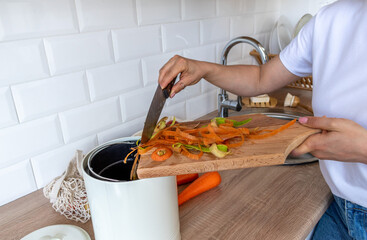 Adult woman puts cleaning of vegetables into compost bucket. People veggie. Home kitchen interior....