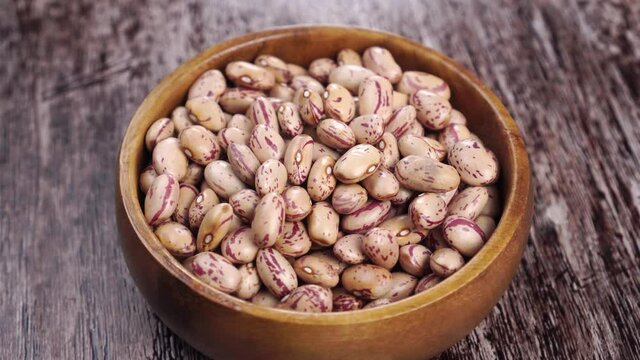 Uncooked dry pinto cranberry beans in a wooden bowl on a rustic wood surface. Rotation. Close up. Vegetable healthy food