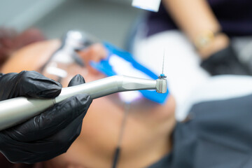 Drill with a tool in the hands of a dentist in black gloves for the treatment of pulpitis, canals in dentistry. Against the background of a patient with glasses