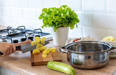 Boy stands in kitchen at home and cuts potatoes with knife on the board. Vegan content.
