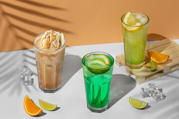 beautiful still life composition with three transparent glasses of summer drink. green lemonade with lime, mint, lemon and citrus on a tropical background with shadows of a palm tree
