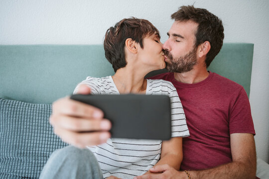 Affectionate couple kissing while taking selfie through smart phone at home
