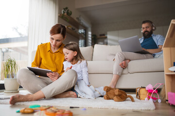 Mother with small daughter using tablet indoors at home, everyday life and home office with child...