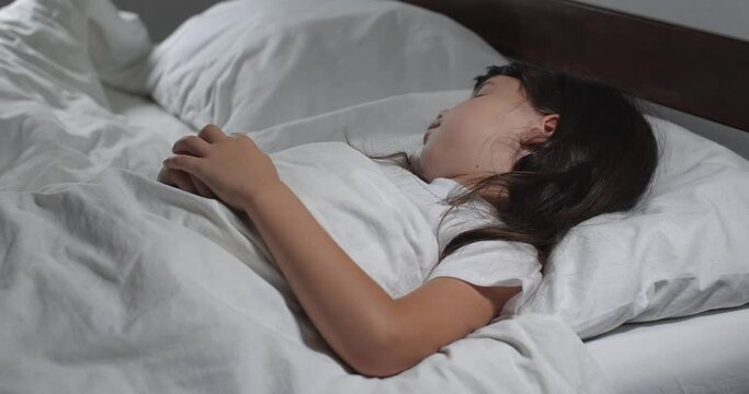 Close up   of little girl 6 years old with long brown hair sleeping  in bed with white linens in light room.  Insomnia concept 4k. Little  child having restless sleep