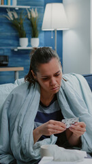 Sick woman looking at bottle of pills and tablets with capsules finding treatment against headache and virus infection. Adult with disease holding medicaments, medicine and vitamins