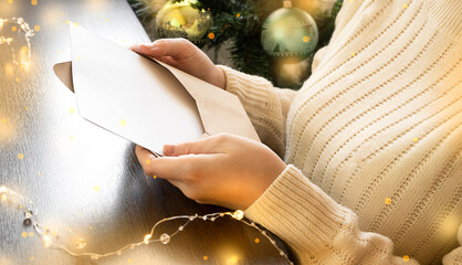 a girl in a sweater sits next to a Christmas tree and reads a letter
