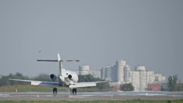 A private plane lands on the runway at the airport with a background on the houses in the city. Slow motion video of a small plane landing.