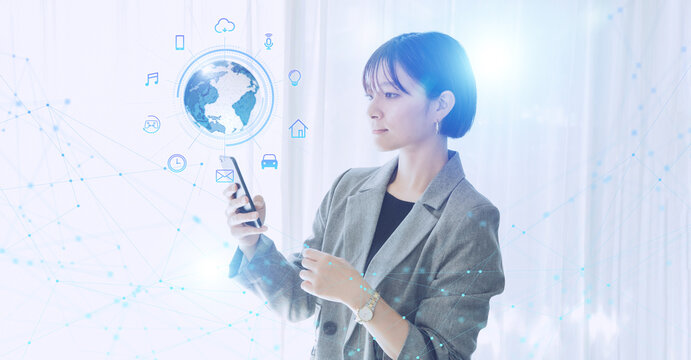 白い明るいオフィスで日本人女性がスマートフォンでIOTを操作するテクノロジーとホログラムのCGグラフィックス