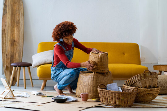 Woman wearing headphones cleaning wicker basket in living room