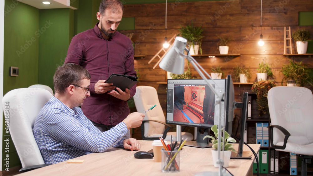 Poster graphic designer working in gaming industry showing new virtual game design to his colleague discuss