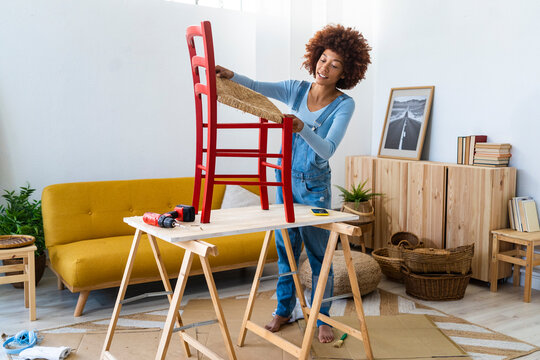 Afro woman restoring wooden chair on table at home