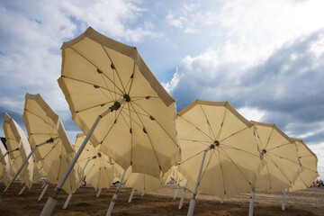 Row of open umbrellas on the beach on the cloudy sky background