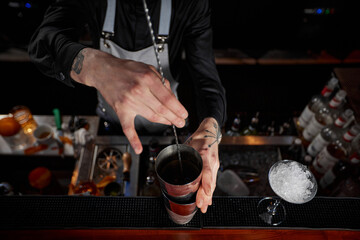 Barman stirring cocktail in shaker with spoon