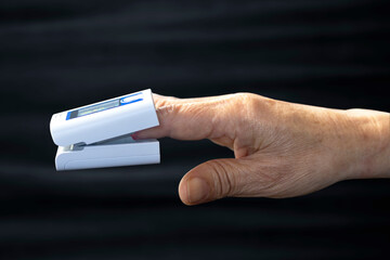 Elderly person's finger and pulse oximeter seen from the side, black background