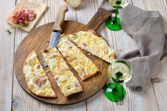 Deftiger Els&auml;sser Flammkuchen mit Zwiebeln, ger&auml;uchertem Speck und kr&auml;ftigem M&uuml;nsterk&auml;se &ndash; Hearty tarte flamb&eacute;e from Alsace with onions, smoked bacon and munster cheese served with Alsatian wine