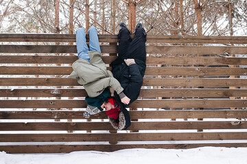 Silly couple kissing while hanging upside down from a wooden fence