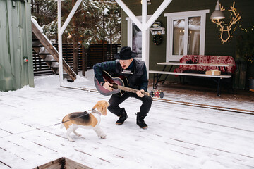 Eccentric musician in a hat and leather jacket playing guitar for a friendly dog