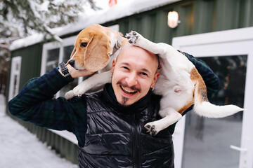 Cheerful bold man playing with a dog, lifting her on his shoulders