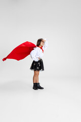 Portrait of beautiful caucasian little girl wearing red cape standing isolated on white studio background with copyspace for ad