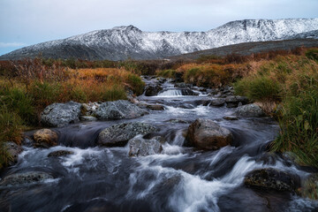 Mountain river with beautiful rifts. Cold water flows quickly over the stones. A snow-capped mountain range can be seen behind. Hiking and travel.