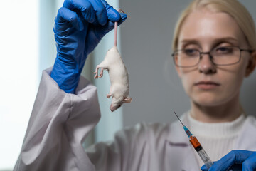 A blonde woman in a white coat and medical gloves takes a blood test from a white experimental...