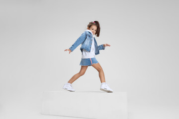 Full-length portrait of smiling girl in casual clothes standing on big box isolated on white studio background. Happy childhood concept.