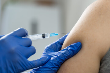 The nurse's hands insert a syringe containing the flu vaccine into the patient's shoulder. Strengthening immunity. Close-up