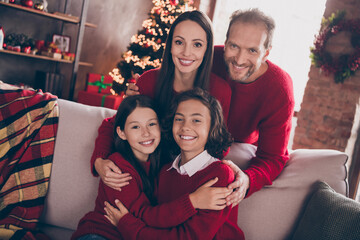 Photo of full family cuddle relax sit on couch wear red jumpers indoors at x-mas
