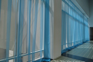 Grandes baies vitrées lumineuses avec voilages bleus.