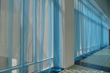 Grandes baies vitrées lumineuses avec voilages bleus.