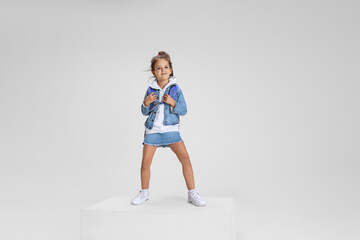 Full-length portrait of smiling girl in casual clothes standing on big box isolated on white studio...