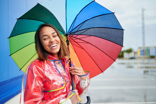 Happy woman wearing raincoat holding multi colored umbrella during rainy season