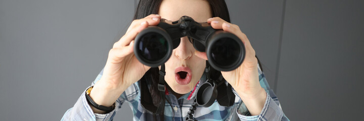 Surprised woman opening her mouth and looking through black professional binoculars