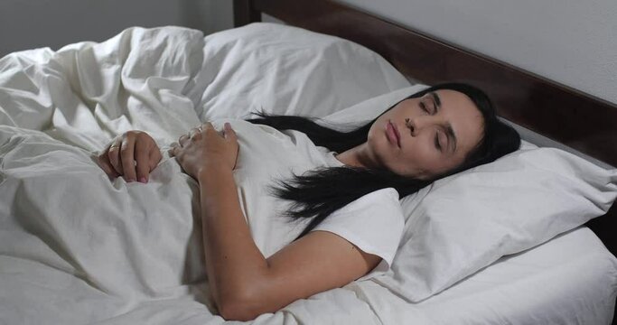Close up of caucasian young woman waking up in bed with white linens in light room.  Woman  waking up but raelizing that it is weekend 