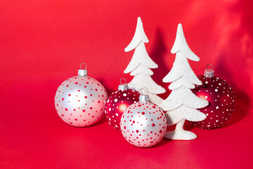 Christmas card with snow-covered white New Year trees and colorful balls on bright red background.