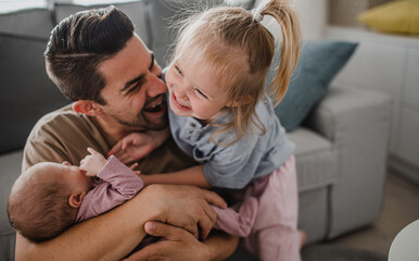 Happy young man taking care of his newborn baby and little daughter indoors at home, paternity...