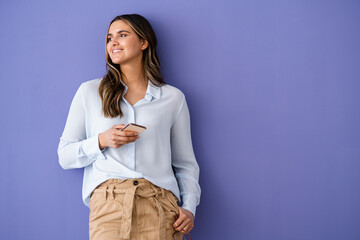 Female business professional holding smart phone while leaning on purple wall