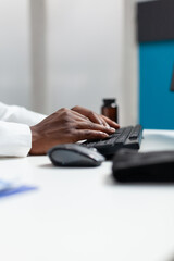 Closeup of african american therapist doctor typing patient healthcare treatment on computer after analyzing disease symptoms. Therapist man working at medical documents in hospital office