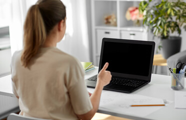 education, online school and distant learning concept - student woman with laptop computer and pencil drawing showing thumbs up at home