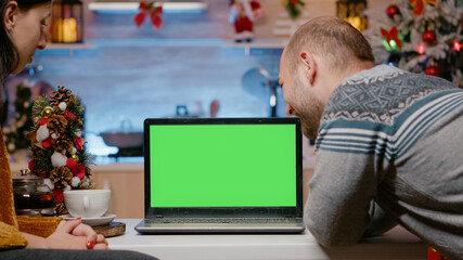 Couple using horizontal green screen on christmas eve looking at laptop. Man and woman watching...