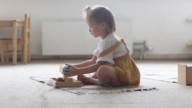 Toddler child girl playing with natural wooden toys on the floor in a bright room, child playing alone, montessori materials and educational toys