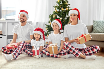 family, winter holidays and people concept - happy mother, father and two daughters in santa hats with christmas gifts at home