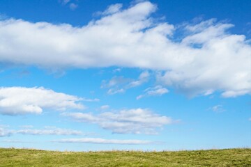 Blue cloudy sky background with green grass, and nobody.  Nice weather theme, freedom concept, feeling of peace emotion, embrace nature idea.
