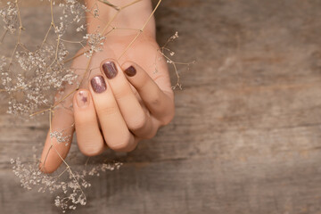 Female hand with glitter brown nail design. Female hand hold autumn flower Brown nail polish...