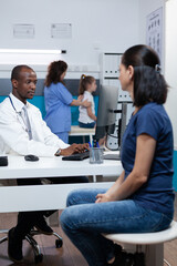 Obraz premium African american pediatrician doctor explaining sickness expertise to patient mother typing medical treatment on computer. Specialist man working in hospital office during clinical appointment