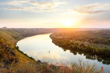 The girl floats on SUP on the river at sunset. Beautiful landscape, girl in the distance