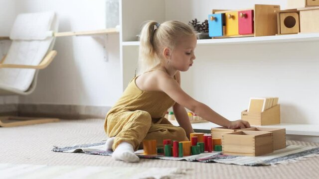 Toddler child girl playing with natural wooden toys on floor in a bright room, the child plays alone, montessori materials and educational toys, developing montessori environment