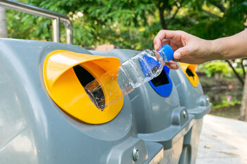 A hand female throwing empty plastic water bottle into to recycling bin at park. Environmental protection concept.