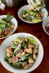 Demonstration of ready-to-serve caesar salad on a rustic wooden table. Tomatoes, twigs, hard cheese shaves. Food preparation technique.