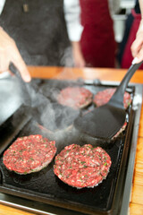 Technique for making burgers at home. The chef presses burger patties on a grill, seasoned with green herbs. Beautiful sparking of steam. home kitchen